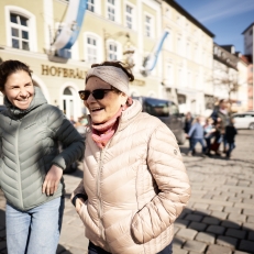 Mutter und Tochter spazieren bei gutem Wetter durch die Stadt und lachen.