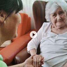 Pflegekraft hält einfühlsam die Hand einer älteren Frau mit weißem Haar, die in einem Sessel sitzt – Symbolbild für Betreuung, Vertrauen und menschliche Nähe im Umgang mit Demenz.