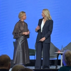 Zwei Frauen stehen auf einer Bühne vor blauem Hintergrund