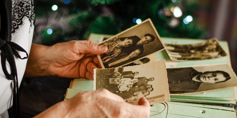 Ältere Person hält alte Schwarz-Weiß-Fotografien in der Hand, im Hintergrund ein Weihnachtsbaum – Symbolbild für Erinnerung, Biografiearbeit und emotionale Momente im Umgang mit Demenz.