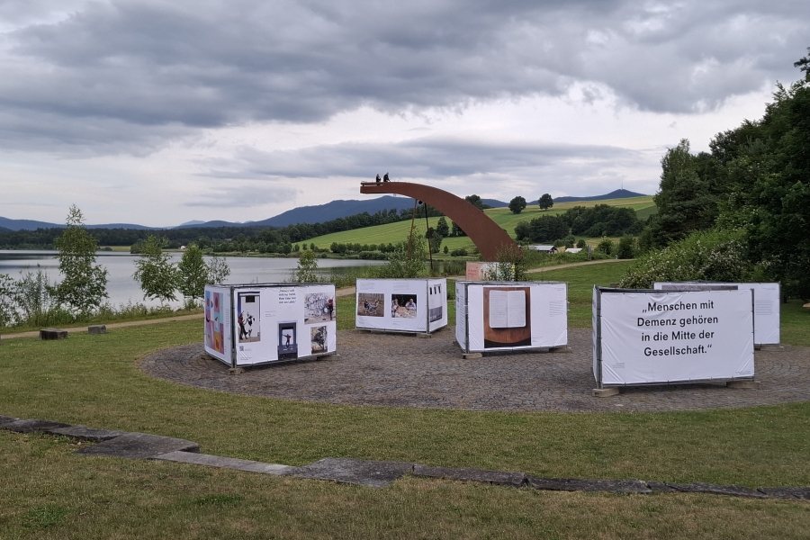 Großformatige Banner der Ausstellung „Demenz neu sehen“ mit emotionalen Fotografien und Zitaten, idyllisch platziert am Drachensee bei Furth im Wald.
