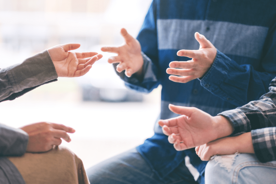 Ausschnitt einer Gesprächssituation in einer Gruppe – mehrere Menschen diskutieren gestikulierend im Kreis, symbolisch für Austausch, Mediation oder Angehörigengespräch.