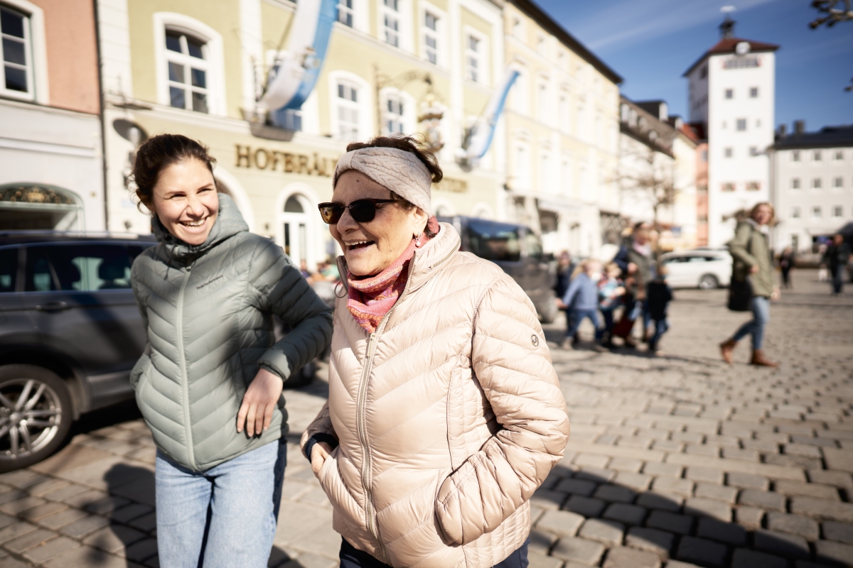Mutter und Tochter spazieren bei gutem Wetter durch die Stadt und lachen.