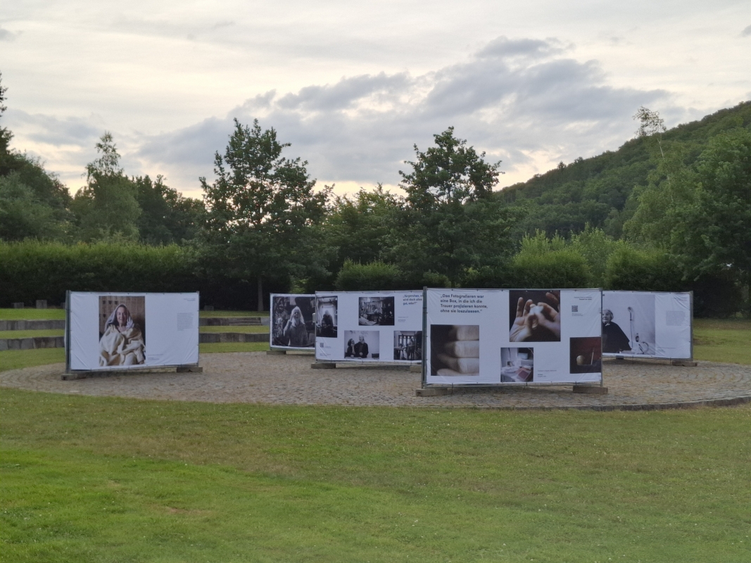 Großformatige Fotografien der Ausstellung „Demenz neu sehen“ auf dem Promenadenplatz in Furth im Wald bei Abendlicht, umgeben von Natur.