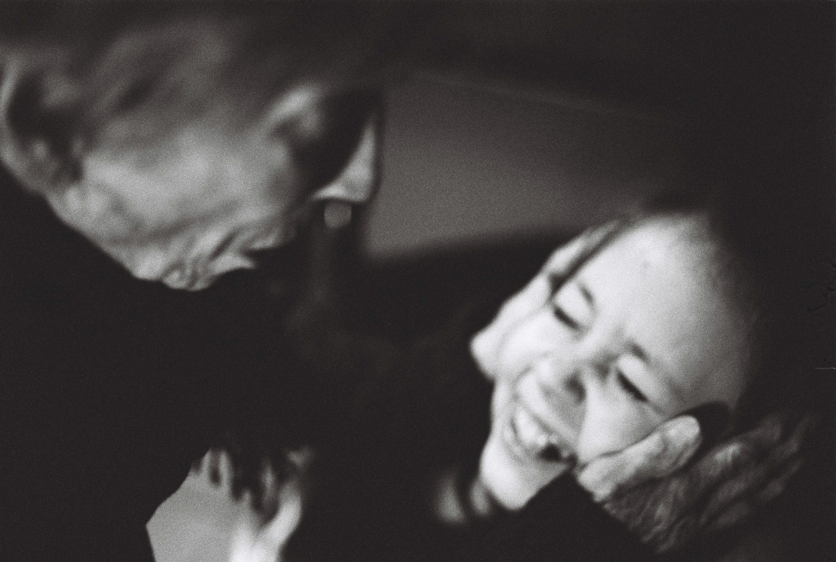 Schwarz-Weiß-Fotografie einer älteren Person, die sanft das Gesicht einer lächelnden jungen Frau in den Händen hält, inniger und emotionaler Moment.