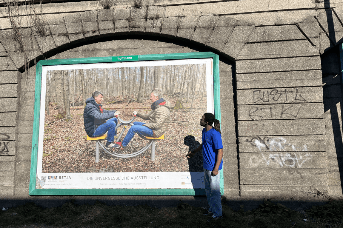 Mann steht vor Plakat der Plakataktion der unvergesslichen Ausstellung Demenz neu sehen