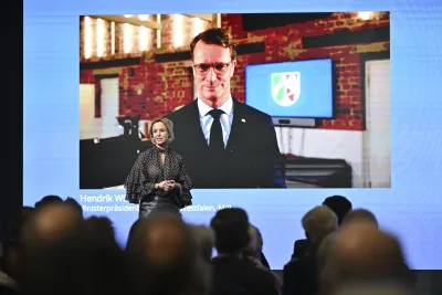 Moderatorin steht auf der Bühne vor einer Leinwand