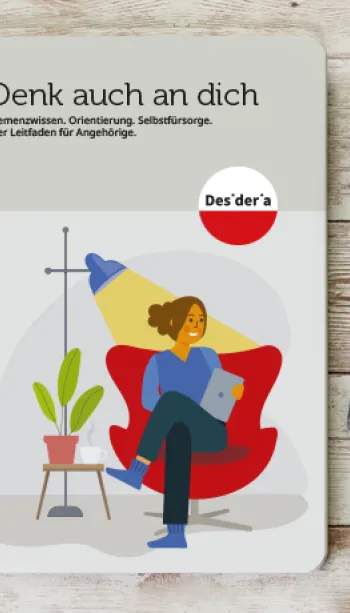 Broschüre 'Demenz neu sehen' von Desideria Care auf Holztisch, daneben Tasse Kaffee und schwarzer Stift.