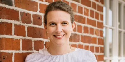 Journalistin und Autorin lehnt an einer Mauer und lächelt in die Kamera.