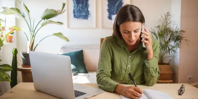 Frau sitzt am Schreibtisch und telefoniert und notiert sich etwas.