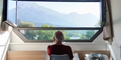 Mann mit Demenz sitzt vor einem Fenster und schaut auf die Berge 