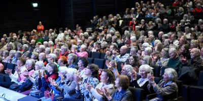 Publikum in einem vollbesetzten Veranstaltungssaal, größtenteils ältere Menschen, applaudierend und aufmerksam – Momentaufnahme eines Vortrags oder Kulturprogramms im Rahmen einer Demenz-Veranstaltung.