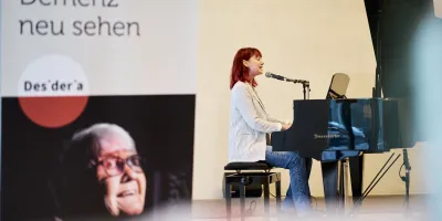 Eine Frau sitzt am Klavier und singt beim Demenz Meet München 2025.