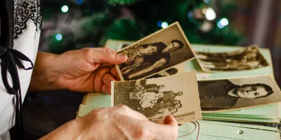Ältere Person hält alte Schwarz-Weiß-Fotografien in der Hand, im Hintergrund ein Weihnachtsbaum – Symbolbild für Erinnerung, Biografiearbeit und emotionale Momente im Umgang mit Demenz.