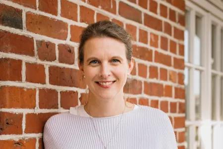 Journalistin und Autorin lehnt an einer Mauer und lächelt in die Kamera.