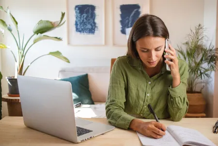 Frau sitzt am Schreibtisch und telefoniert und notiert sich etwas.