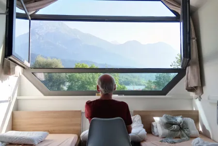 Mann mit Demenz sitzt vor einem Fenster und schaut auf die Berge 