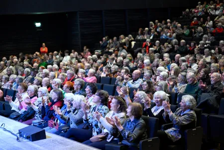Publikum in einem vollbesetzten Veranstaltungssaal, größtenteils ältere Menschen, applaudierend und aufmerksam – Momentaufnahme eines Vortrags oder Kulturprogramms im Rahmen einer Demenz-Veranstaltung.