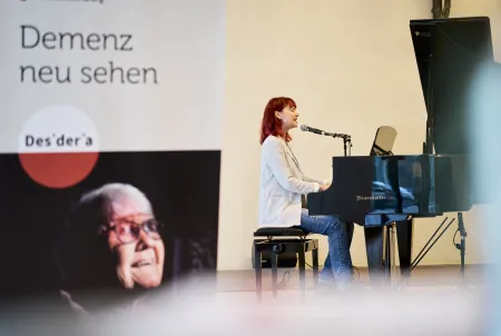 Eine Frau sitzt am Klavier und singt beim Demenz Meet München 2025.