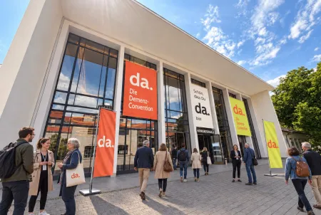 Eingang der alten Kongresshalle München, mit Besuchern und bunten Plakaten der da.