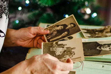 Ältere Person hält alte Schwarz-Weiß-Fotografien in der Hand, im Hintergrund ein Weihnachtsbaum – Symbolbild für Erinnerung, Biografiearbeit und emotionale Momente im Umgang mit Demenz.