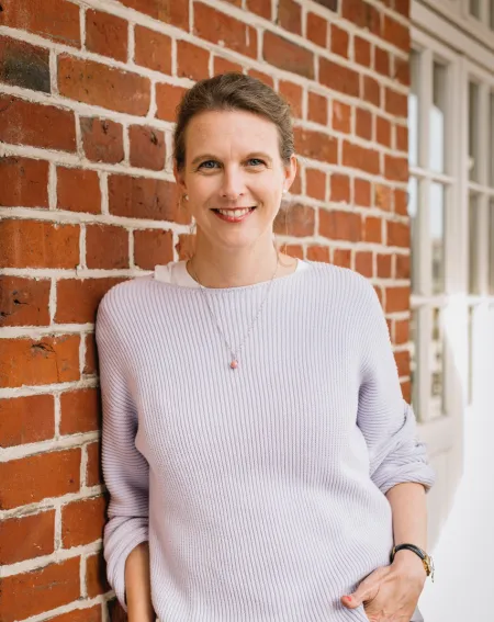 Journalistin und Autorin lehnt an einer Mauer und lächelt in die Kamera.